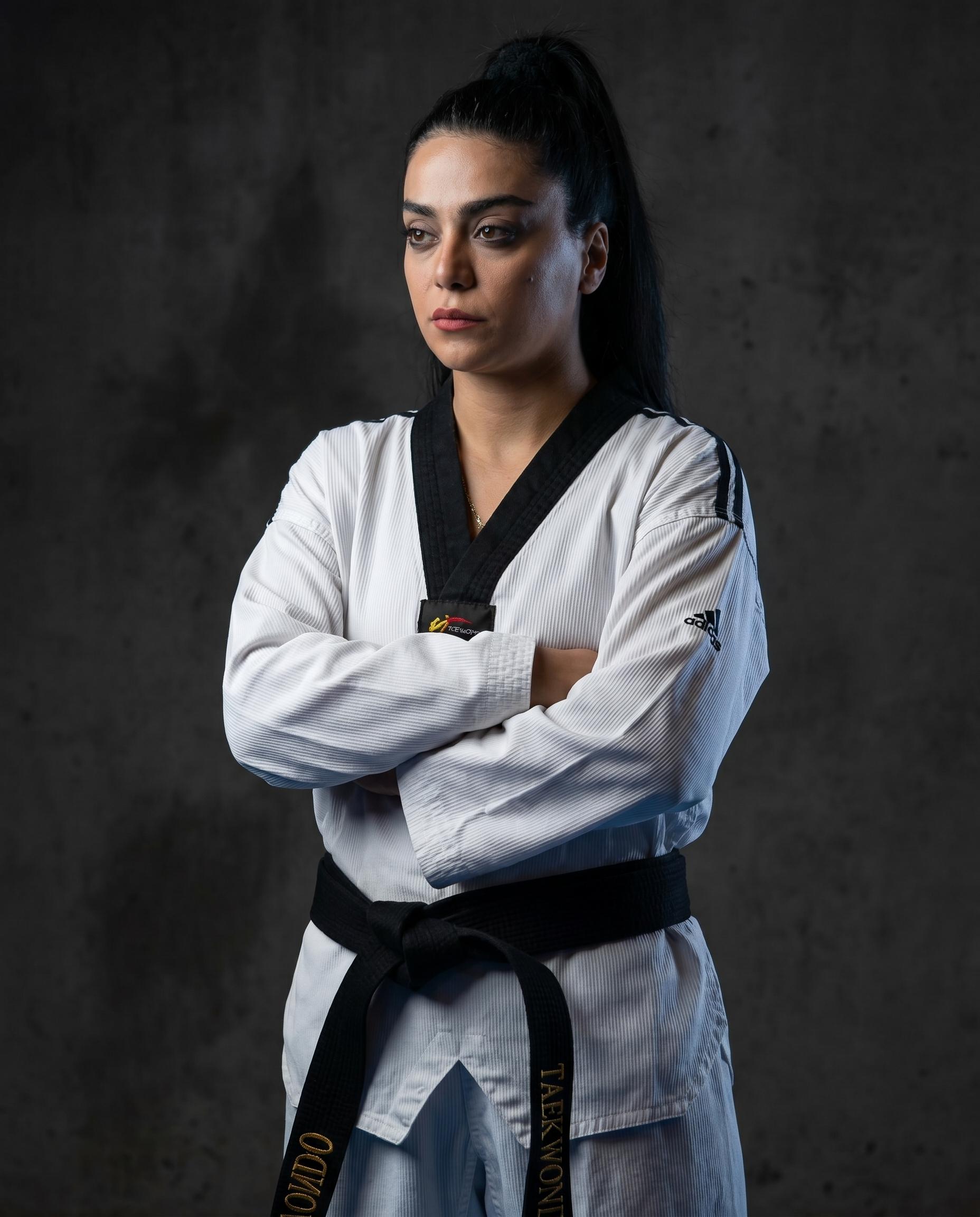 Portrait of lead trainer Azadeh in her dobok and black belt, arms crossed